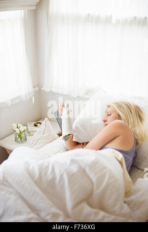 Blonde woman reading in a bed with white linen. Stock Photo