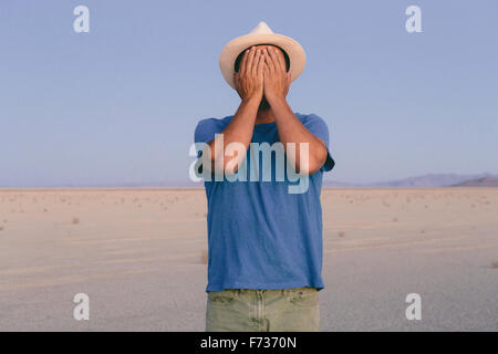 A man in an open desert landscape covering his face with his hands. Stock Photo