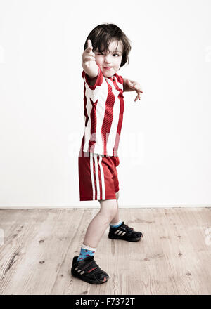 A boy in red and white striped shirt and football shorts standing pointing at the camera. Stock Photo