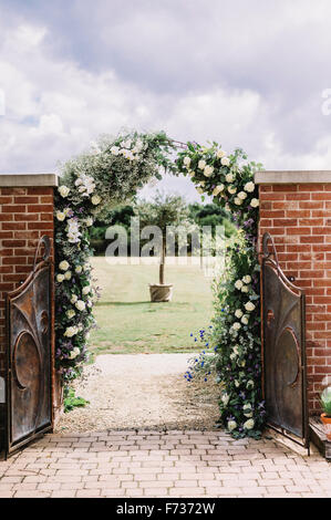 A door in a wall, and a white rose arch in a garden, with a view to a sundial. Stock Photo