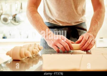 A baker working on a floured surface, rolling up dough squares into croissant shapes before baking. Stock Photo