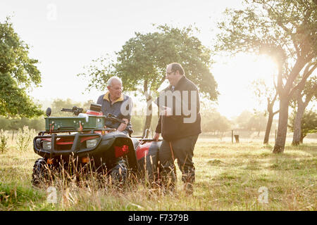 Two men, a farmer and a man with a clipboard, by a quadbike in an orchard. Stock Photo