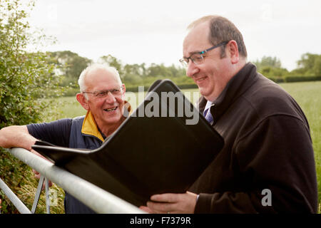 Two men standing looking over a farm gate, one with an open file and paperwork. Stock Photo