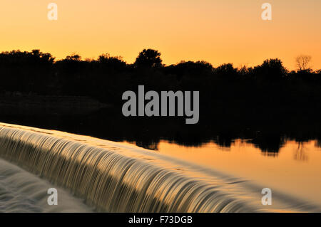 Tranquil water turns to white water as it flows over a dam in the Fox River in South Elgin, Illinois at sunset. Stock Photo