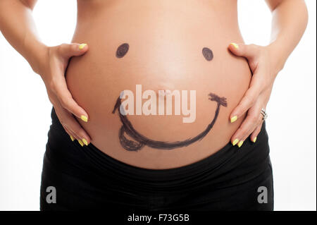 A smiley face drawn on a woman's pregnant belly. Stock Photo