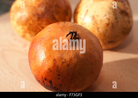 Three pomegranates over a wood table, a winter fruit. Stock Photo