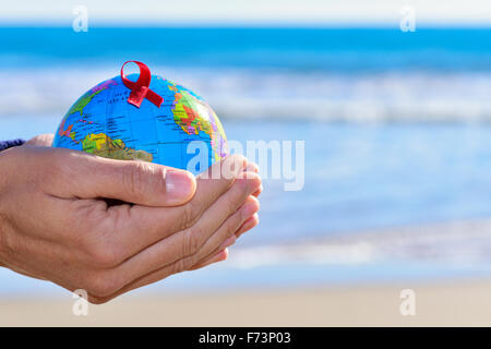 closeup of the hands of a young caucasian man holding a world globe with a red ribbon, for the fight against AIDS Stock Photo