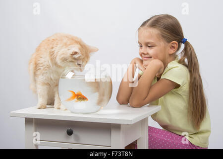 Happy six year old girl and a cat sitting at the table at the fishbowl with goldfish Stock Photo