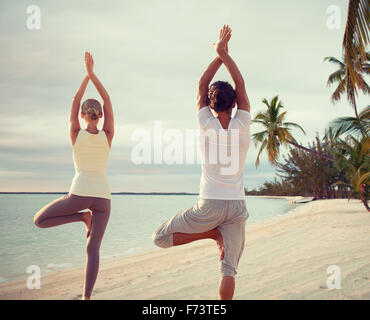 couple making yoga exercises on beach from back Stock Photo