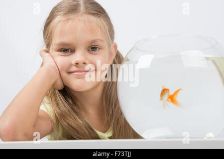 Happy six year old girl sits at a table at the fishbowl with goldfish Stock Photo