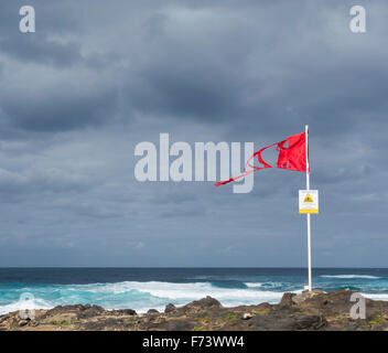 Tattered red flag and strong currents sign on windy beach in Spain Stock Photo