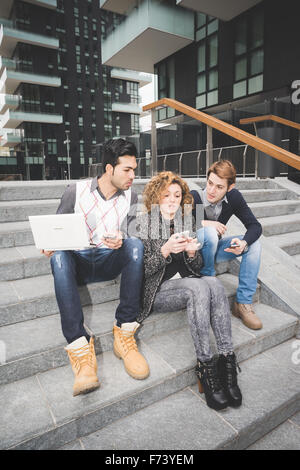 Multiracial business people working outdoor in town connected with technological devices sitting on a staircase, talking to each other - business, work, team concept Stock Photo