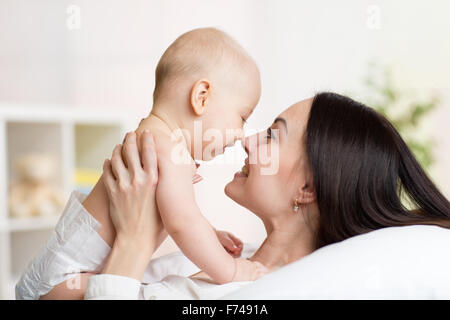Mother and baby laugh and play lying on bed Stock Photo