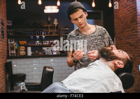 Handsome barber shaving bearded man with straight razor in barbershop Stock Photo