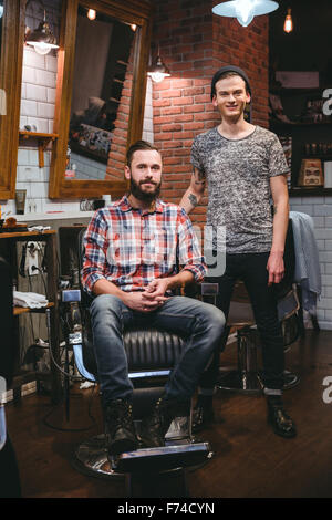 Portrait of young modern barber and his handsome content bearded client in barbershop Stock Photo