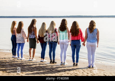Eight teenage girls having fun standing side by side holding hands while looking out to sea along Broughty Ferry beach in Dundee, UK