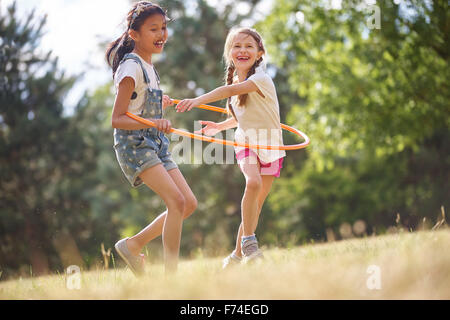 Two happy girls play with hula hoop in summer Stock Photo