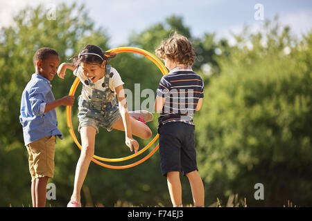 Girl jumps thourgh hula hoop while her friends hold it Stock Photo