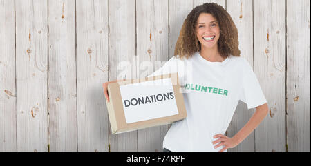 Composite image of smiling volunteer holding a box of donations with hand on hip Stock Photo