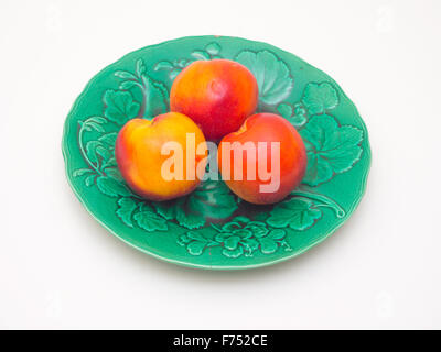 Three ripe late season Nectarines on a green plate Stock Photo