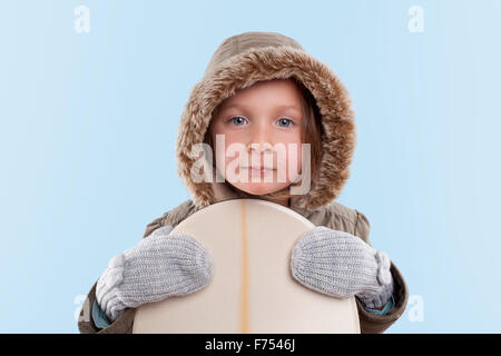 Little snowboarder. Cute little girl holding snowboard against light blue background. Stock Photo