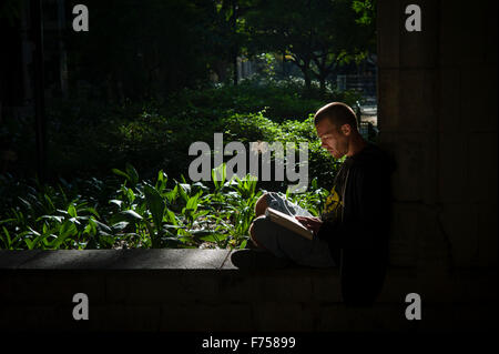 A man sits in the shade reading a book in a garden in the Barcelonetta district of bacelona (Taken in Barcelona, Spain) Stock Photo