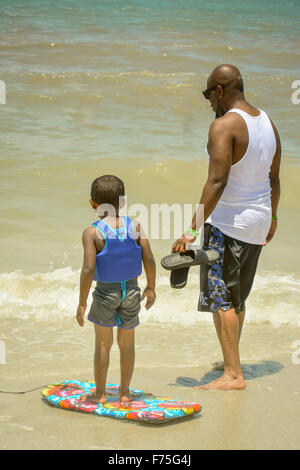 Rear view of African American boy wearing a life vest with his boogie board and an adult African American man at the shoreline Stock Photo