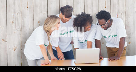 Composite image of smiling volunteers working together on a laptop Stock Photo