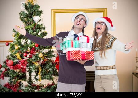 Composite image of smiling man and woman wearing santa hats and holding gifts Stock Photo