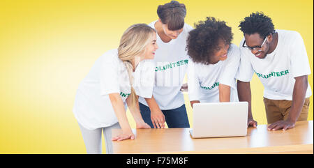 Composite image of smiling volunteers working together on a laptop Stock Photo