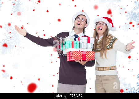 Composite image of smiling man and woman wearing santa hats and holding gifts Stock Photo