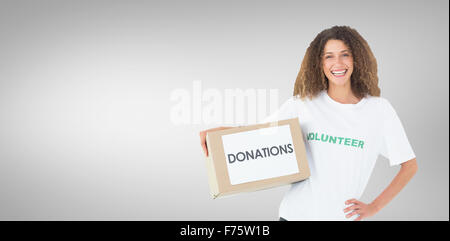 Composite image of smiling volunteer holding a box of donations with hand on hip Stock Photo