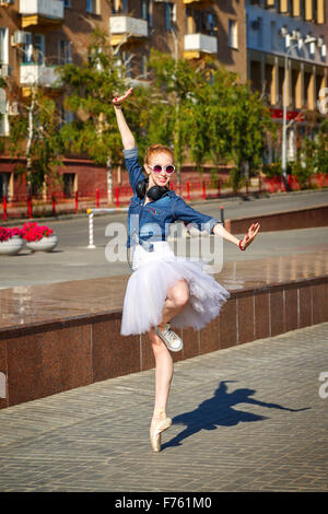 Cute ballerina dancing in the street. A girl wearing a tutu and pointes. Girl listening to music on headphones. Stock Photo