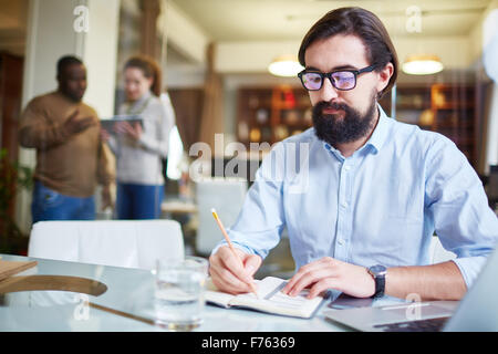 Modern employee writing working plan in notepad Stock Photo