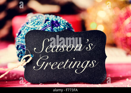 closeup of a black label with the text seasons greetings and on a rustic wooden surface with some different christmas ornaments Stock Photo