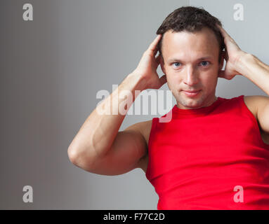 Young Caucasian man in red sporty shirt does an exercise on the abdominal muscles Stock Photo