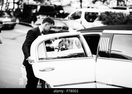 Groom open door of limousine and take hand to bride Stock Photo