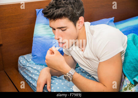 Close Up of Attractive Young Man Lying in Bed and Taking Cough Syrup - Sick Man Taking Medicine While Lying in Bed Recuperating Stock Photo