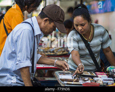 Bangkok, Bangkok, Thailand. 27th Nov, 2015. An amulet vendor points out an amulet to a potential customer at her street stall on Maharat Road. Hundreds of vendors sell amulet and Buddhist religious paraphernalia to people in the Amulet Market, a popular tourist attraction along Maharat Road north of the Grand Palace near Wat Maharat in Bangkok. Bangkok municipal officials announced that they are closing the market and forcing vendors to relocate to an area about one hour outside of Bangkok. The closing of the amulet market is the latest in a series of municipal efforts to close and evict stre Stock Photo