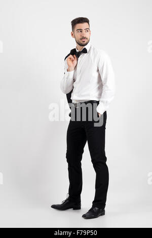 Side view of elegant man holding suit jacket over his shoulder looking away with hands in pockets. Full body length portrait Stock Photo