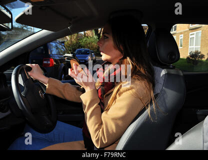 Young woman female driving a car while using her mobile smart phone breaking the law in the UK (posed by a model) Stock Photo