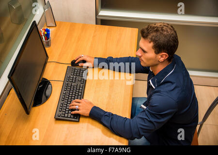 Successful handsome young businessman sitting at his desk in the office smiling and looking at the computer screen Stock Photo