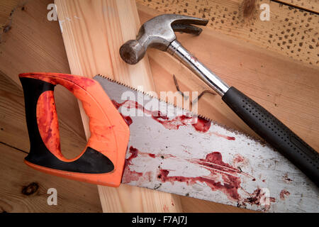 A hammer and carpenters saw with blood after a diy accident UK Stock Photo