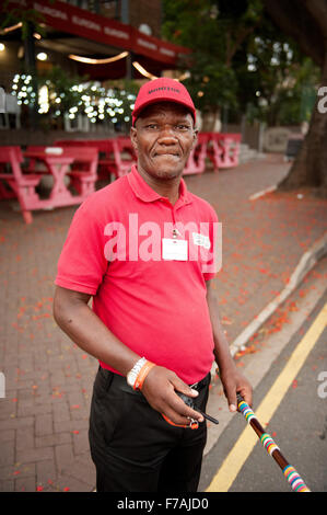 A car guard with a traditional Zulu war club, at the sidewalk cafe along Durban's Florida Road entertainment area.  South Africa Stock Photo