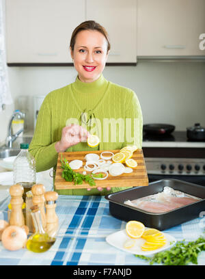 Smiling housewife cooking filleted fish at kitchen Stock Photo