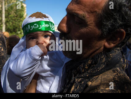 Iranian Shiite Man Covered In Mud Holding His Baby During Ashura Day, Kurdistan Province, Bijar, Iran Stock Photo