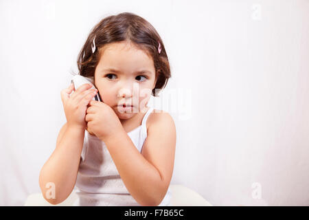 Little girl with ear talking electronic thermometer taking herself the temperature. Isolated over white background Stock Photo