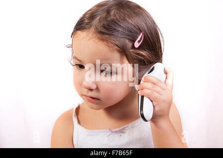 Little girl with ear talking electronic thermometer taking herself the temperature. Isolated over white background Stock Photo