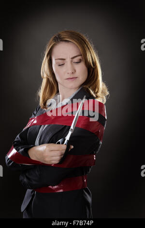 business woman wrapped up in red tape about to cut herself free Stock Photo