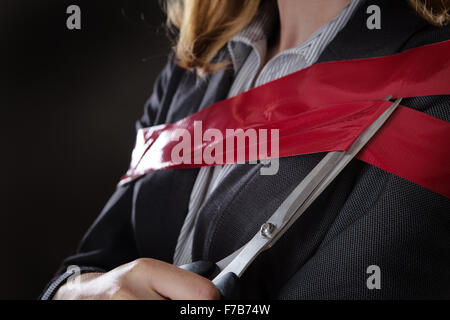 business woman wrapped up in red tape about to cut herself free Stock Photo